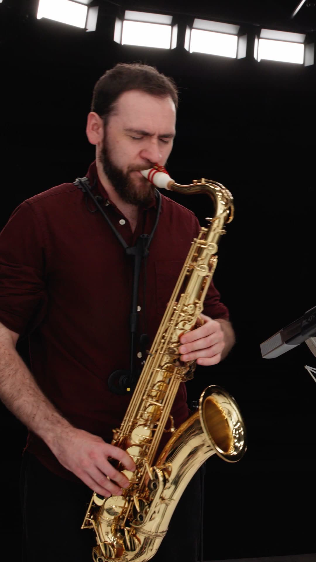 Jordan Smart playing the saxophone in the ConcertLab studio, Nick Smart at the piano behind him